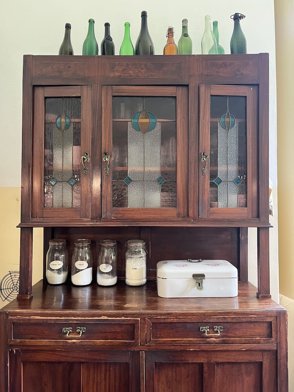 An antique kitchen cabinet with stained glass doors and old green bottles