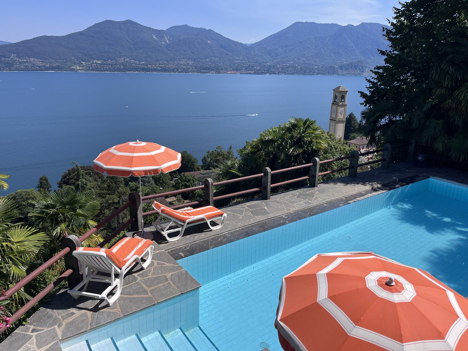 The pool with striped orange parasols and loungers above the lake and the church tower